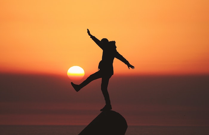 Person balancing on a stone in the sunset