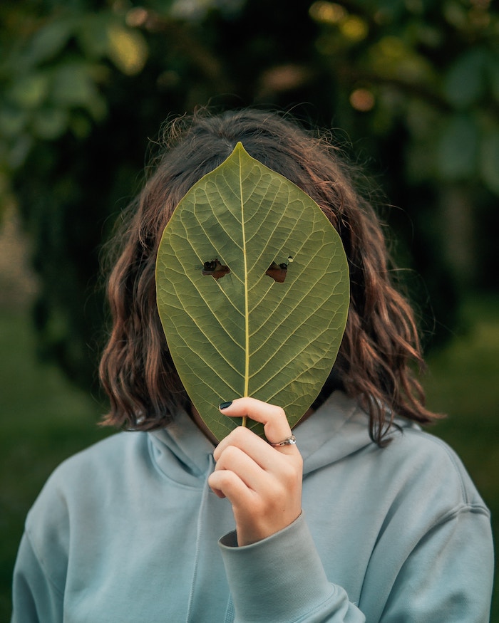 Person holding a leaf as mask in front of the face