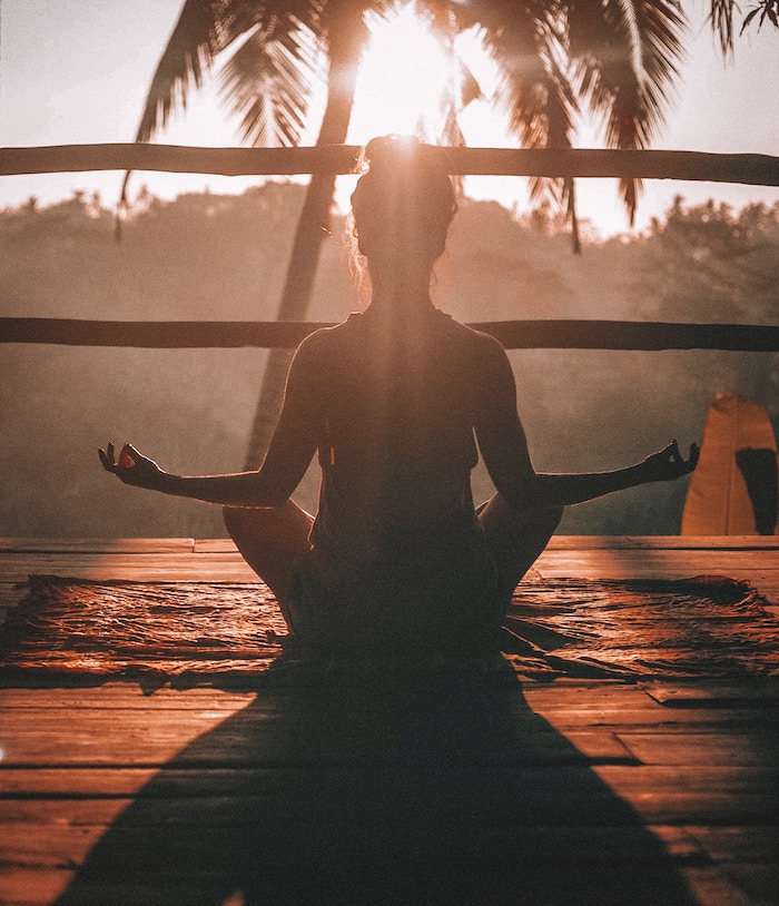 Woman doing yoga on a deck under a palm tree