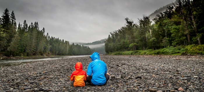 A parent and a kid sitting next to a river