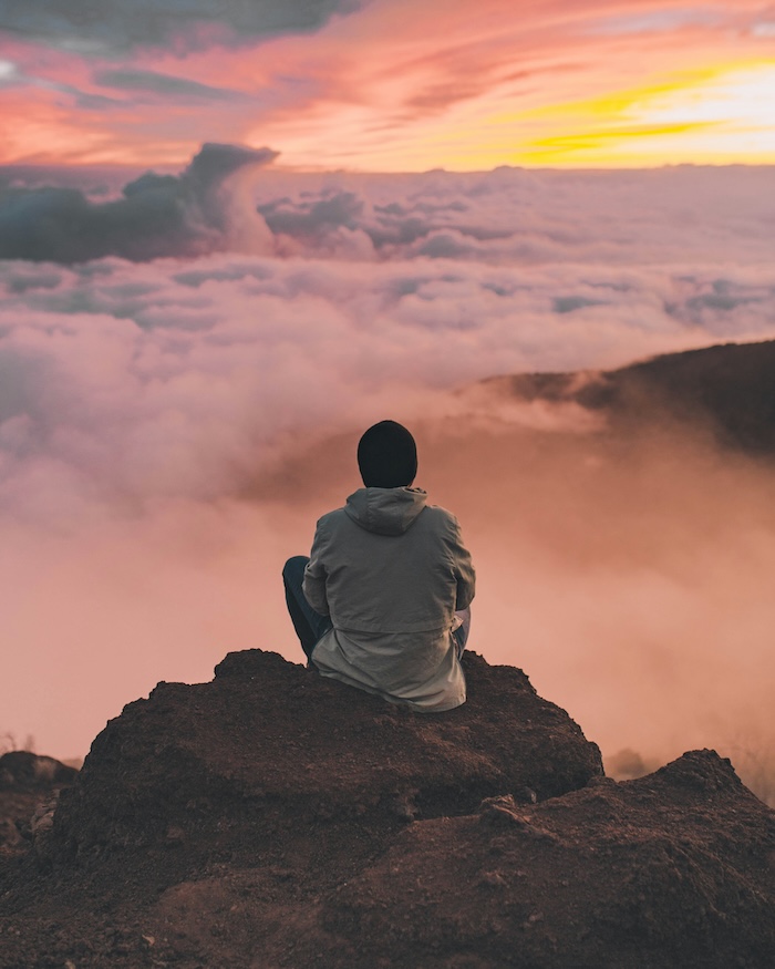 Man sitting at a cliff and looking over clouds